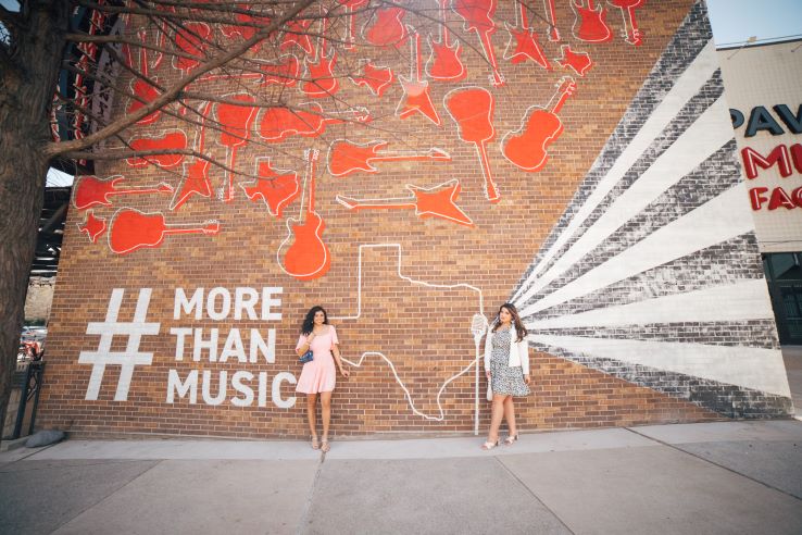 Two young women standing in front of a mural outside of Toyota Music Factory